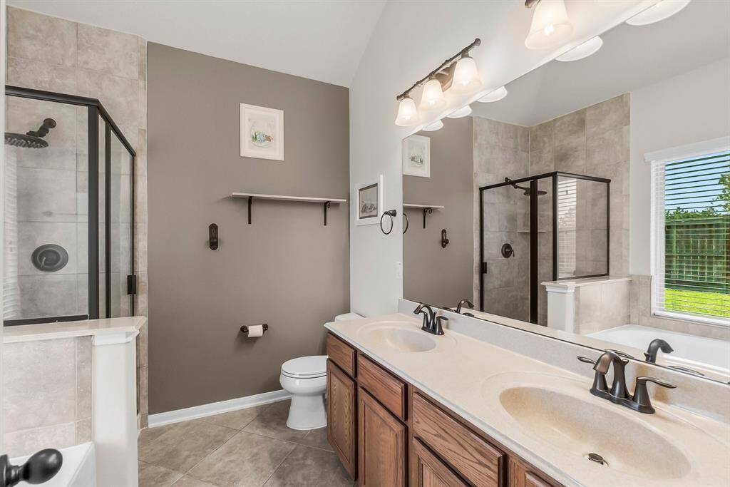 This bathroom features a double vanity with elegant fixtures, a glass-enclosed shower, a separate bathtub, and ample natural light from a large window.