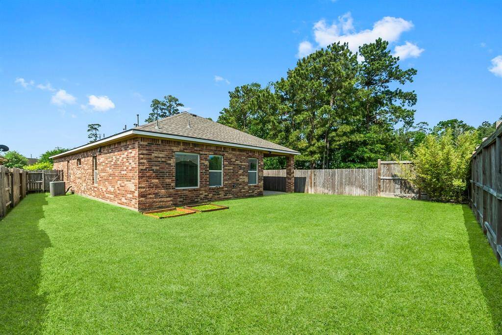 This photo showcases a spacious backyard with lush green grass, a brick house, and a wooden fence providing privacy, perfect for outdoor activities and relaxation.