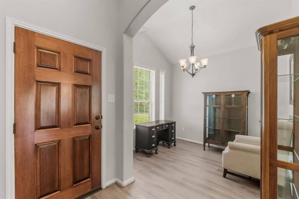 This inviting entryway leads into a bright room with large windows, elegant light fixture, and stylish vinyl flooring, ideal for a home office or sitting area.