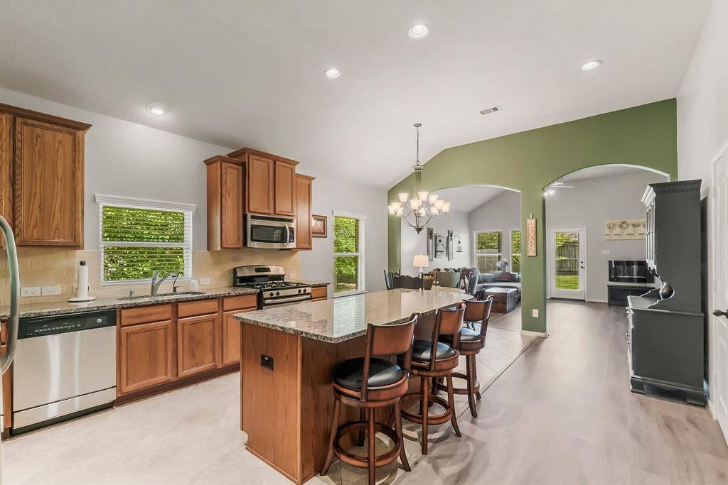 This open-concept kitchen features modern stainless steel appliances, granite countertops, and a central island with bar seating. The space seamlessly connects to a cozy living area with large windows that provide natural light and a view of the backyard.