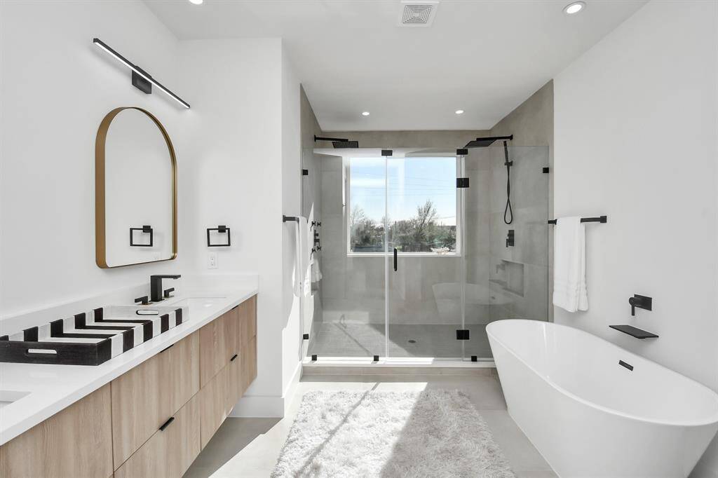 Primary bathroom offers a spa-like retreat offers a freestanding soaking tub alongside a large, frameless glass-enclosed shower with dual rain shower heads.