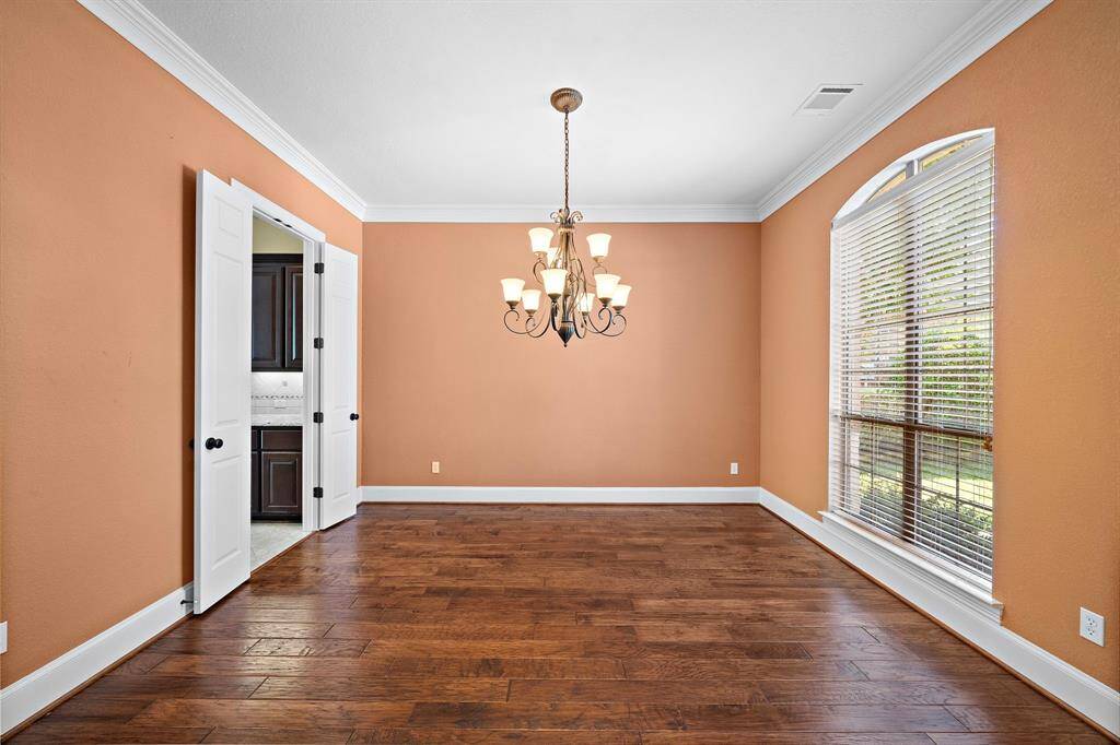 This dining room features warm peach walls, a stylish chandelier, and large windows for ample natural light. It has elegant hardwood floors and white trim, with double doors leading to another space. Perfect for gatherings.