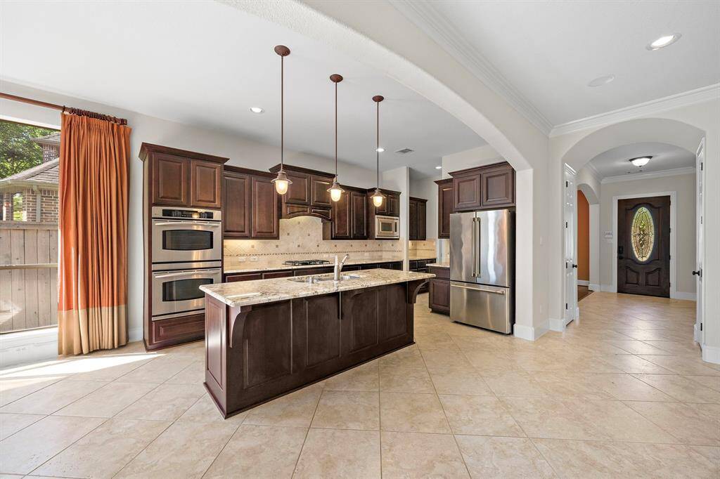 This kitchen features elegant wood cabinetry, granite countertops, and stainless steel appliances. The large island provides ample space for cooking and entertaining, while pendant lighting adds a warm touch. An arched entryway leads to the rest of the home, and a window offers natural light.
