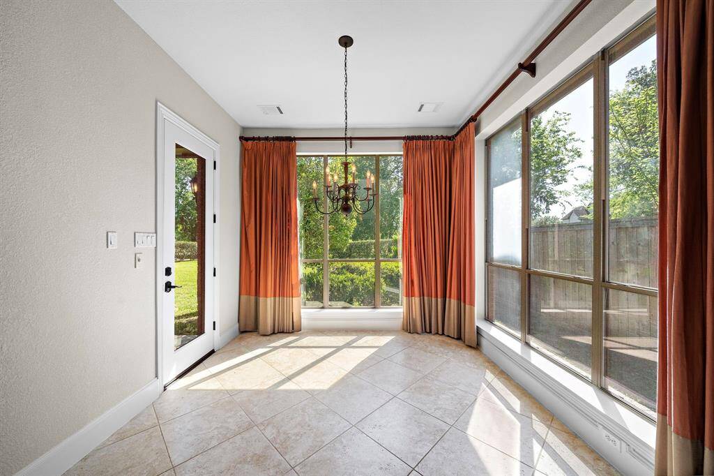 Bright sunroom with large windows, elegant tile flooring, and a central chandelier. Offers ample natural light and views of the garden, perfect for relaxation.