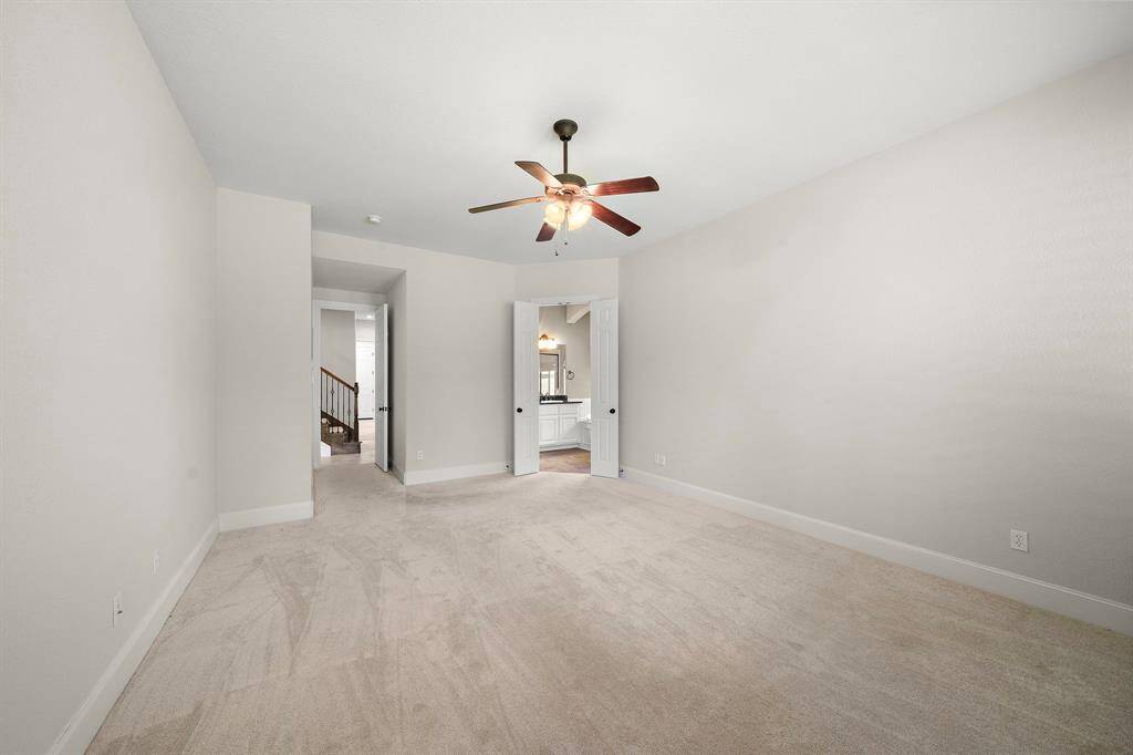 This spacious, carpeted bedroom features neutral walls, a ceiling fan, and ample natural light. It leads to an adjacent bathroom, enhancing convenience and privacy.