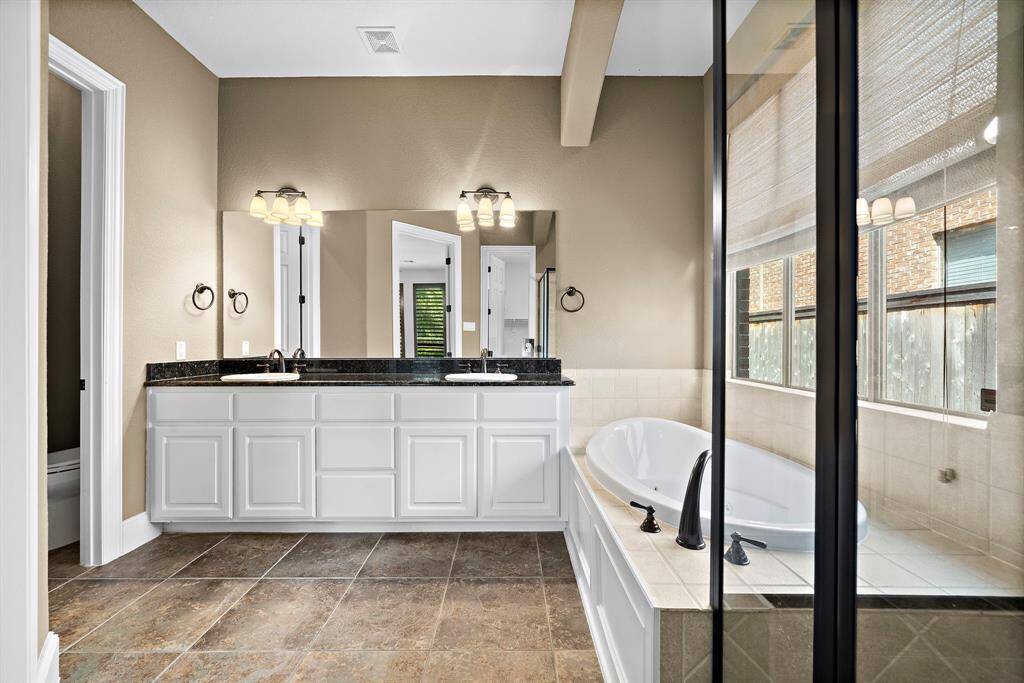 This bathroom features a spacious layout with a double vanity, large mirrors, and ample lighting. It includes a luxurious soaking tub next to a glass-enclosed shower, creating a relaxing and elegant atmosphere.