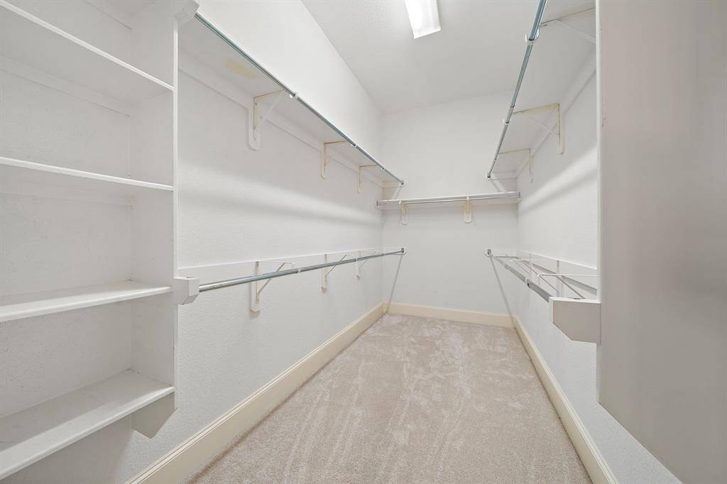 This photo shows a spacious walk-in closet with multiple shelves and hanging rods, offering ample storage space. The carpeted floor and bright lighting provide a clean and welcoming atmosphere.