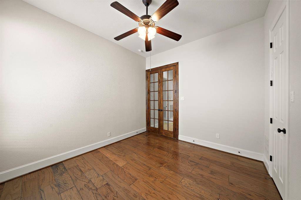 This room features hardwood flooring, a ceiling fan with lights, and French doors, offering a cozy and functional space ideal for a study or small bedroom.