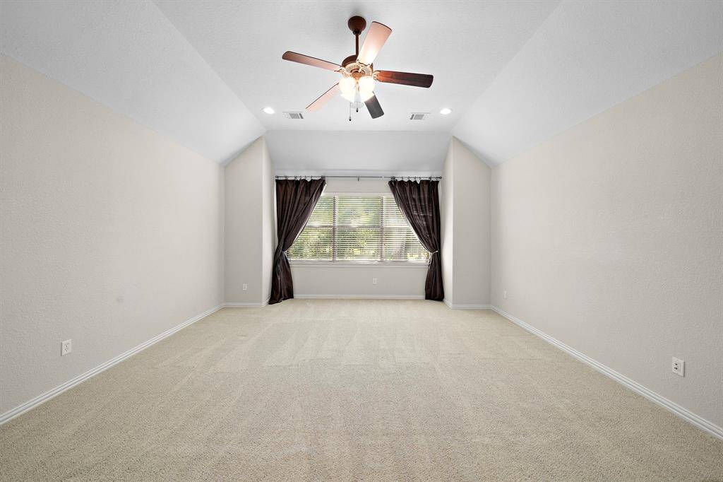 Spacious, bright room with neutral walls, plush carpeting, and a ceiling fan. Features a large window with drapes, offering plenty of natural light.