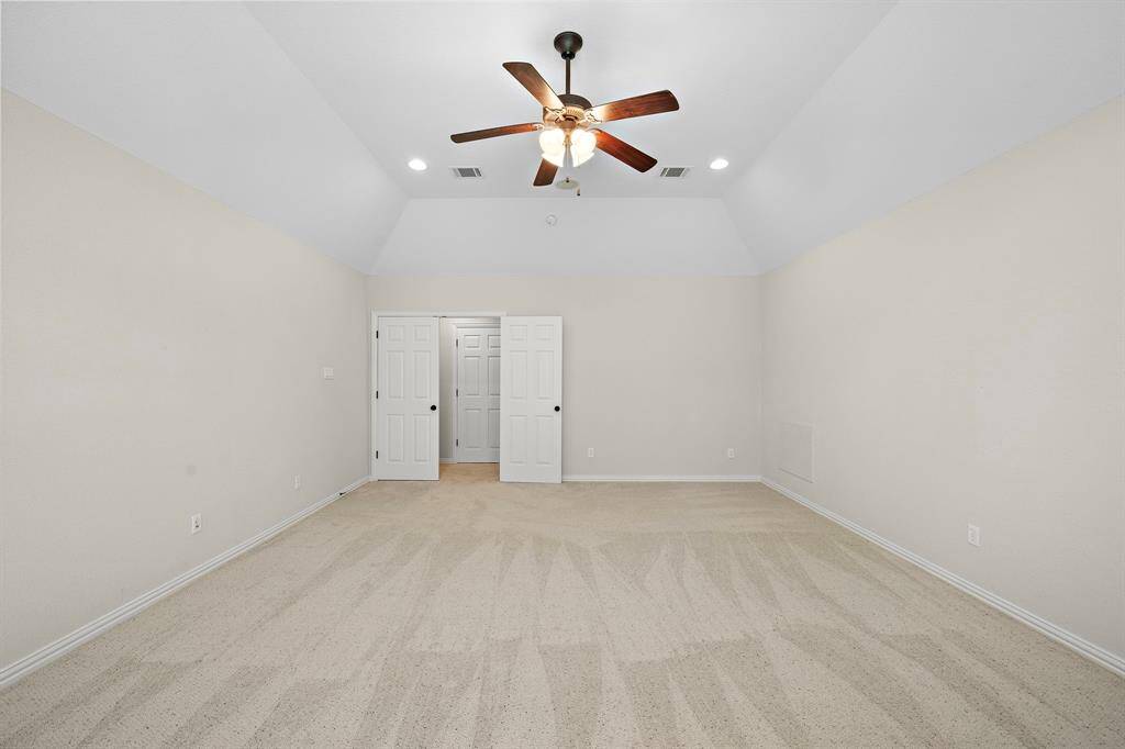 Spacious room with neutral walls and carpet, featuring a ceiling fan and recessed lighting. There's a double-door entry, leading to additional space or storage. Ideal for a master bedroom or large living area.