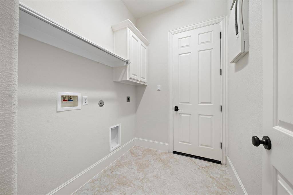 This photo shows a laundry room with tiled flooring, a built-in cabinet, and space for a washer and dryer. It features a hanging rod and a white door, offering a clean and functional space.