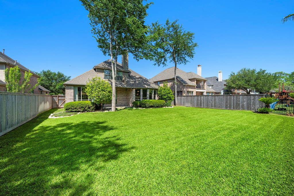 Spacious backyard with lush green lawn, mature trees, and privacy fencing surrounding a charming brick home. Ideal for outdoor activities and entertaining.