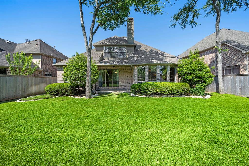 This photo showcases a charming home with a well-maintained lawn, mature trees, and a large patio area. The house features a brick exterior and large windows, providing a welcoming, light-filled atmosphere.