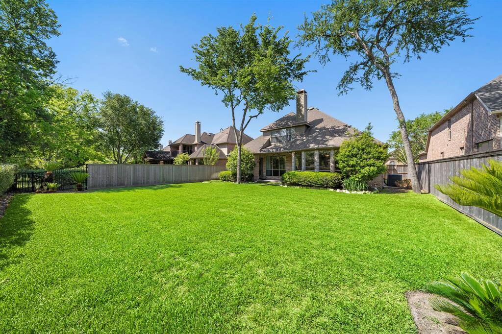 Spacious backyard with lush green lawn and mature trees, offering privacy and ample space for outdoor activities. The house features a charming exterior with a covered patio, perfect for relaxation and entertaining.