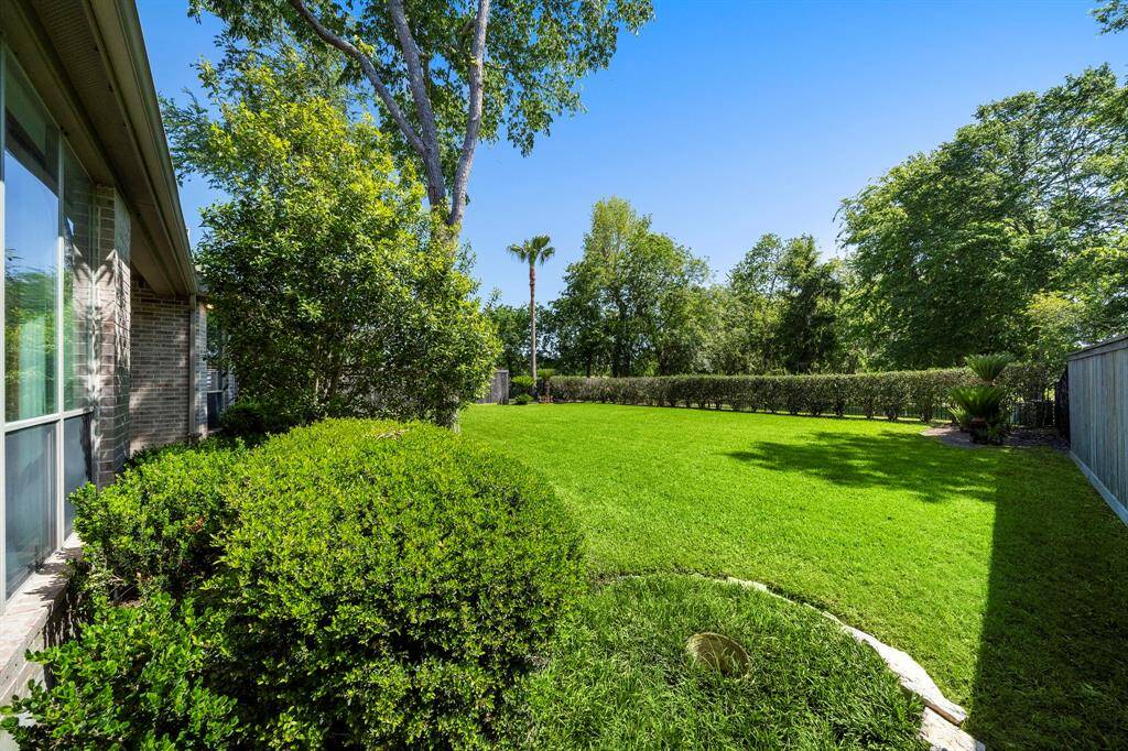 This photo showcases a spacious, well-maintained backyard with lush green grass, mature trees, and privacy hedges, offering a serene outdoor space.