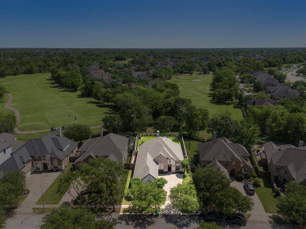 This aerial photo showcases a charming home with a spacious yard, nestled in a tranquil neighborhood. It offers direct views of a lush golf course, providing a serene and picturesque setting.