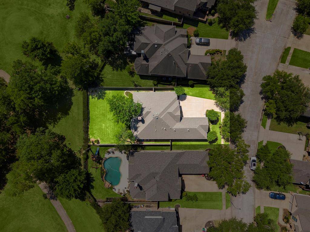 This aerial photo showcases a spacious, well-maintained property with a large backyard, lush greenery, and a private pool. The home is situated in a quiet neighborhood, offering ample driveway space and proximity to a golf course.
