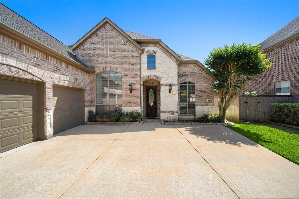 This photo showcases a charming brick home with a two-car garage. The front features large windows, a welcoming arched entryway, and a neatly landscaped yard with a tree and greenery. The driveway offers ample space, and the exterior has a classic, well-maintained look.
