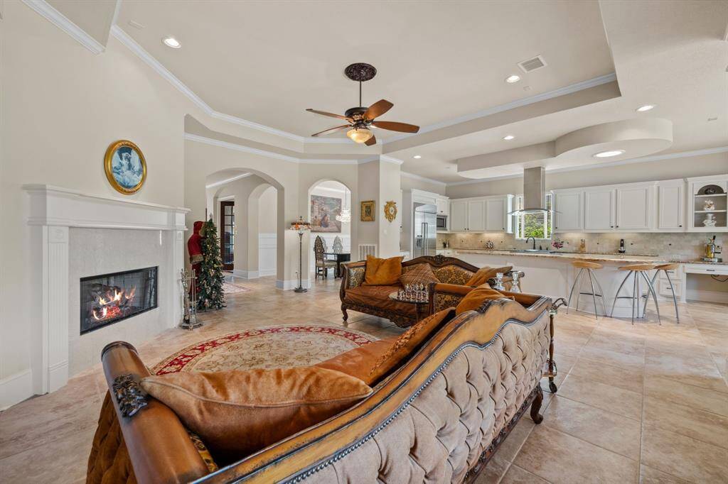 A spacious, open-concept kitchen and living area with large windows providing ample natural light. The kitchen features a modern island with granite countertops and stainless steel appliances, while the living area includes a cozy fireplace and built-in shelving. Neutral tones and elegant finishes create a welcoming atmosphere.