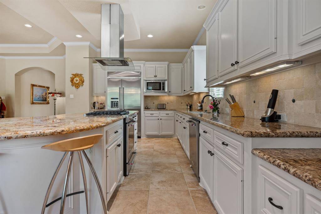 This kitchen features elegant cabinetry, granite countertops, and a central island with bar seating. Stainless steel appliances and a modern range hood enhance functionality, while the neutral tile flooring and ample natural light create a warm, inviting atmosphere.