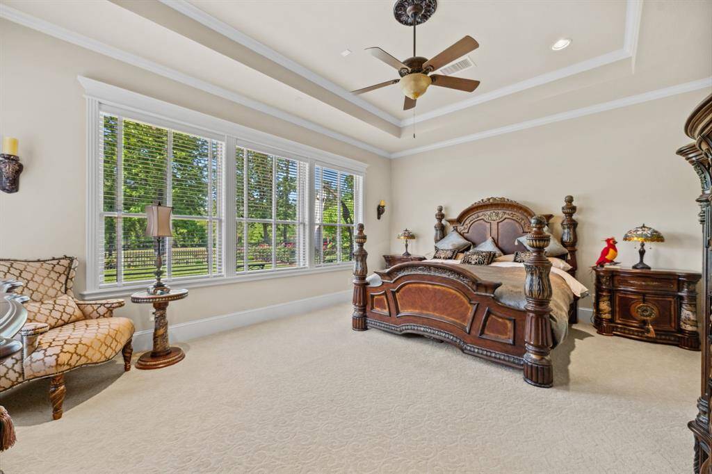 Retreat to this spacious and serene primary suite, featuring elegant tray ceilings, plush carpeting, and a wall of windows that fill the room with natural light and tranquil views. The rich wood furnishings add a touch of timeless sophistication to this peaceful escape.