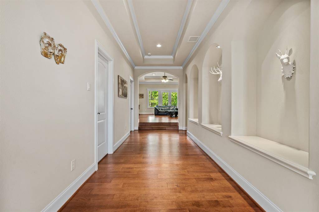 This beautifully detailed hallway features custom arch niches, elegant ceiling accents, and rich wood flooring. It offers a seamless flow that leads directly into the second-floor living/gameroom area, creating a warm and inviting transition between spaces.