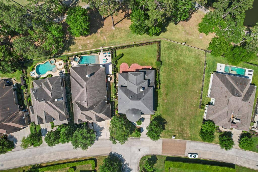 This aerial photo shows a spacious, well-maintained home with a large backyard. The property is surrounded by other upscale homes, each with private pools. There's ample green space and mature trees, providing a serene and private atmosphere.