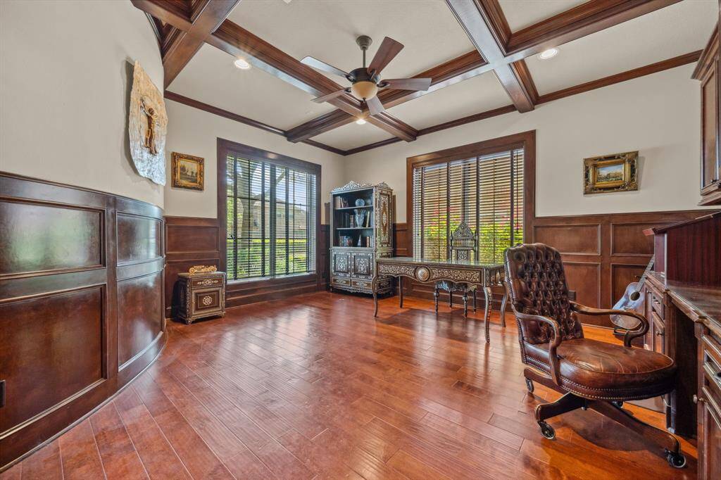 This sophisticated home office showcases rich wood flooring, custom wainscoting, and elegant ceiling beams for a timeless executive feel. Expansive windows allow for abundant natural light, creating an inspiring space perfect for work or study.