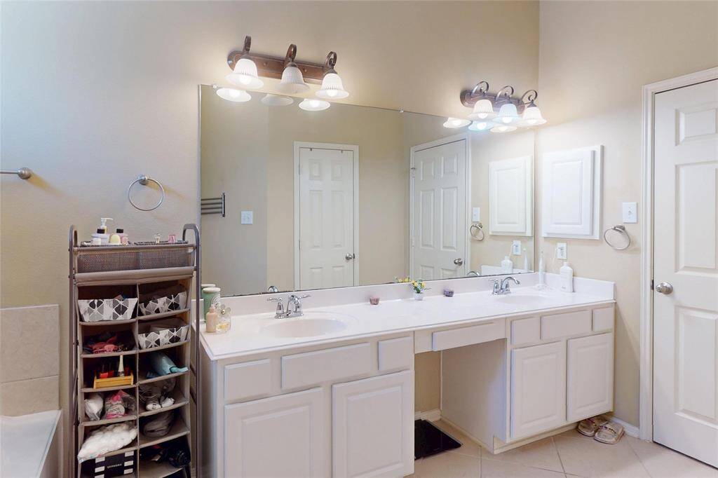 This primary bathroom features dual sinks with ample counter space, large mirrors, and modern light fixtures. It includes built-in cabinetry for storage and has a neutral color palette, offering a clean and spacious feel.