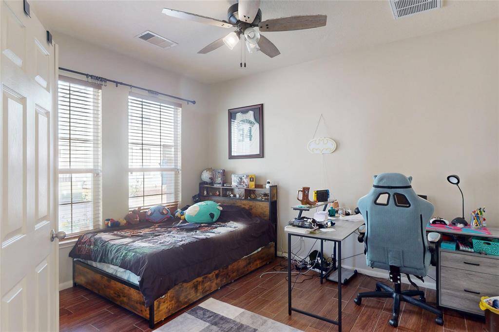 Cozy first floor bedroom with large windows for natural light, wood flooring, and ceiling fan and ensuite bathroom. Features space for a single bed, gaming/office area, and personalized decor.
