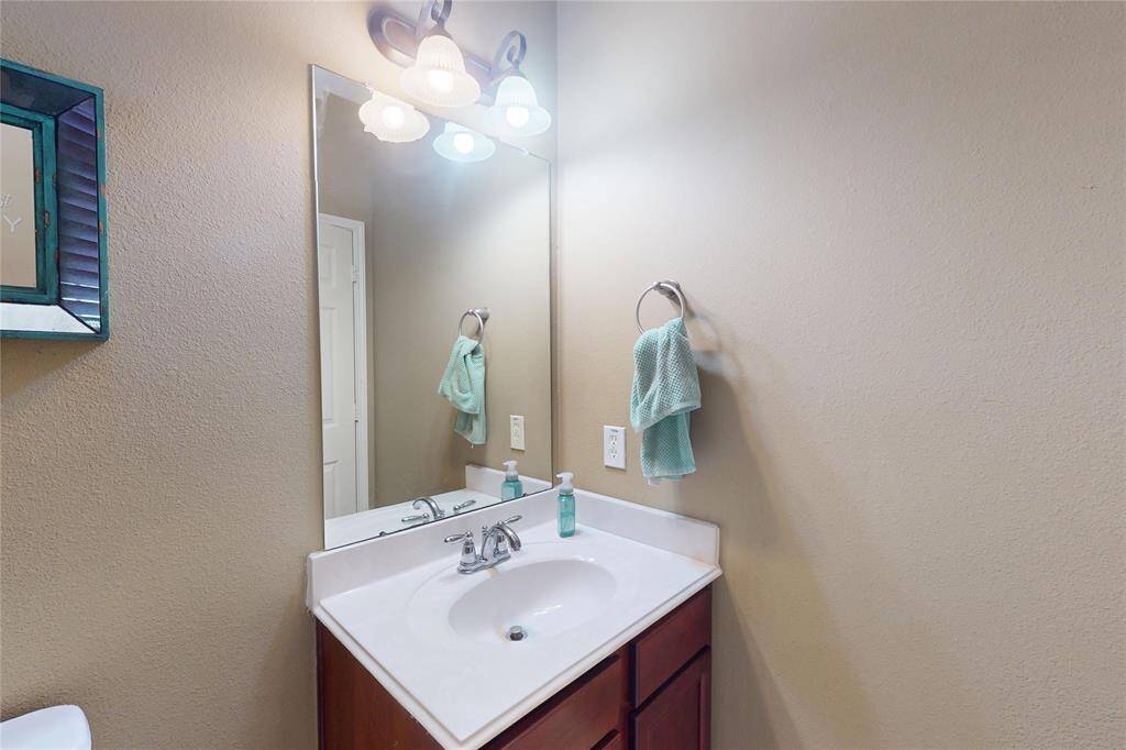 The half-bath on second floor with a corner vanity, featuring a single sink and a large mirror. The space is well-lit with overhead lighting, and there's a towel ring and soap dispenser for convenience.