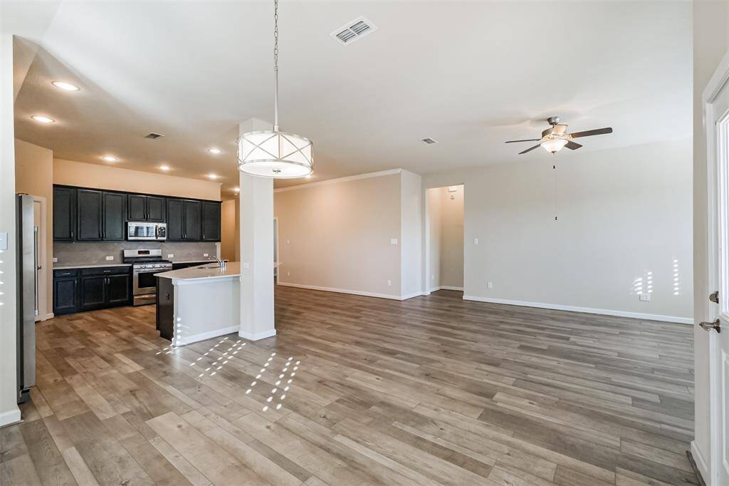 This open-concept living area features hardwood flooring, a modern kitchen with dark cabinetry and stainless steel appliances, a central island, and recessed lighting. The space is bright and airy, with a ceiling fan and neutral walls, perfect for a comfortable and inviting home environment.