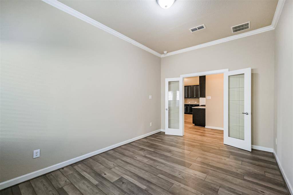 The office/study or flex room is bright with light wood flooring and neutral walls, featuring a ceiling light and double glass doors.