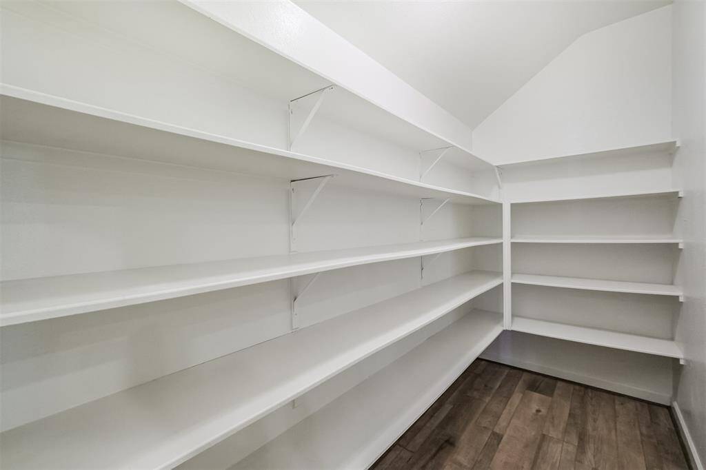Spacious pantry with ample white shelving and wood flooring, perfect for organized storage.