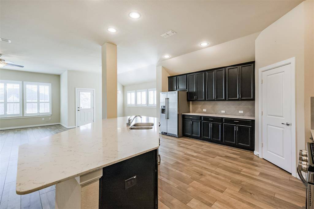 This photo showcases a bright, open-concept kitchen and living area. The kitchen features dark cabinetry, modern appliances, and light countertops with an island. The space is complemented by wood flooring and ample natural light from large windows.