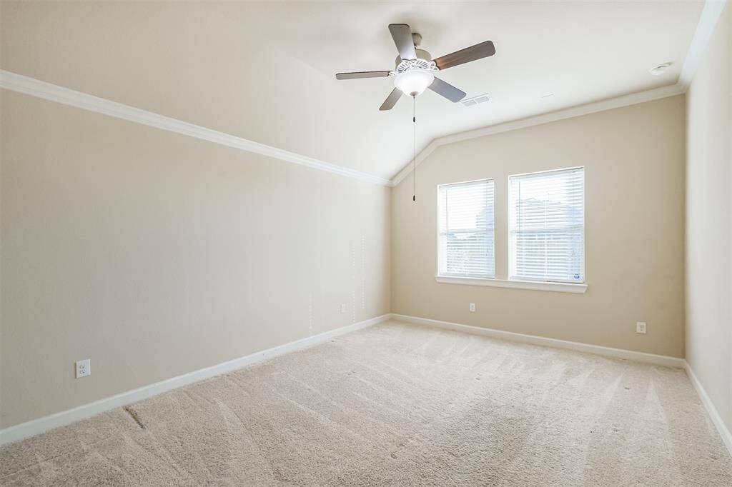 Another angle of this bright, spacious primary bedroom featuring a vaulted ceiling with a ceiling fan, neutral carpet, and two large windows allowing plenty of natural light.