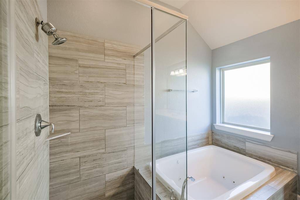 This primary bath retreat features a modern shower with sleek, glass doors and stylish tile work. It includes a luxurious built-in jetted tub, perfect for relaxation, complemented by a large, frosted window for natural light.