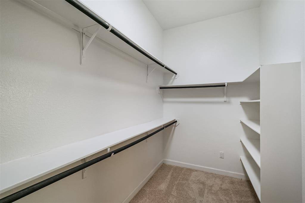 Spacious walk-in closet with multiple hanging rods and built-in shelves, offering ample storage space. Neutral walls and carpet create a clean, versatile look.