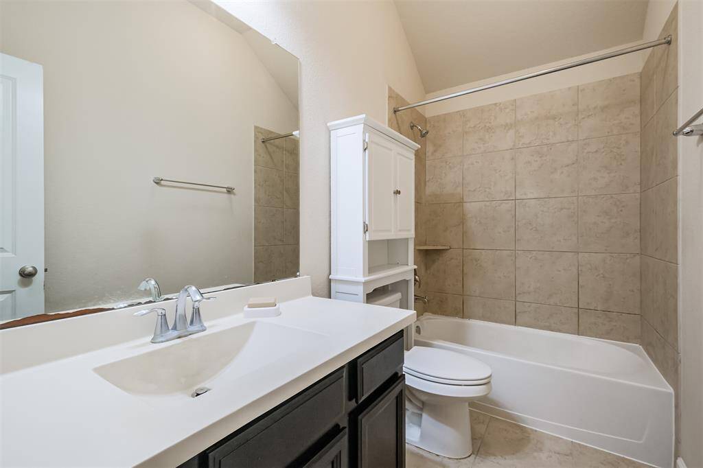 This secondary bathroom features a clean, modern design with a large mirror, white sink, and dark cabinetry. It includes a bathtub with beige tile surround and a built-in storage unit. It's located between the two secondary bedrooms.