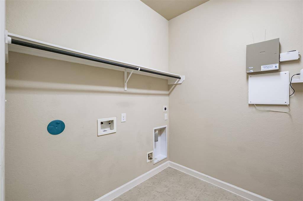 This clean and spacious laundry room is perfect with hookups for a washer and dryer and has a wall-mounted shelf for additional storage and neutral walls, providing a practical and organized space for laundry tasks.