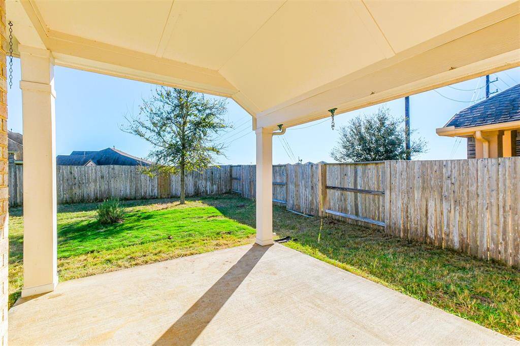 This back porch is so relaxing and showcases a view of a fenced backyard. The space features a well-maintained lawn with a few trees, providing a private and inviting outdoor area.