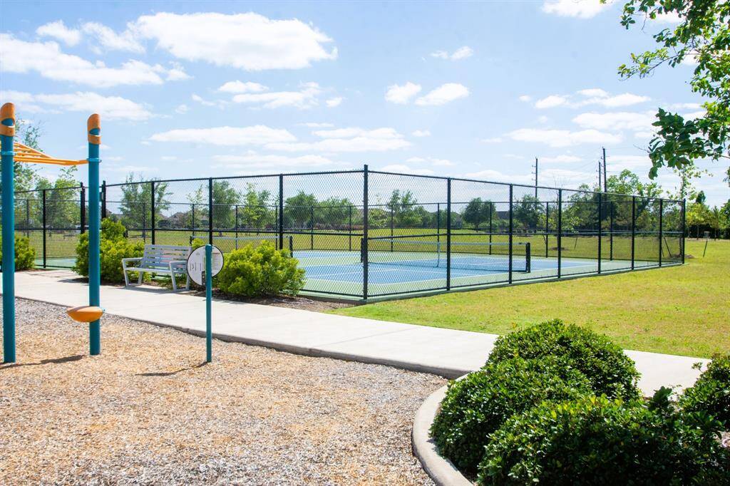 The photo showcases one of the many community recreational areas featuring a fenced pickleball court, a playground with play equipment, benches, and well-maintained landscaping, ideal for families and outdoor activities.