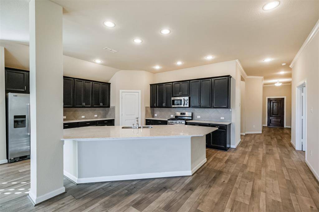 This kitchen features modern appliances, dark cabinetry, and a spacious island with a light countertop, complemented by wood-look flooring and recessed lighting.