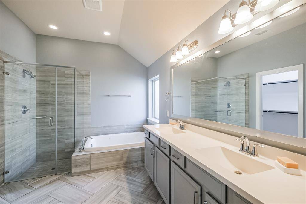 This modern bathroom features a spacious layout with a glass-enclosed shower, a luxurious soaking tub, dual sinks with a large mirror, and elegant tile flooring.