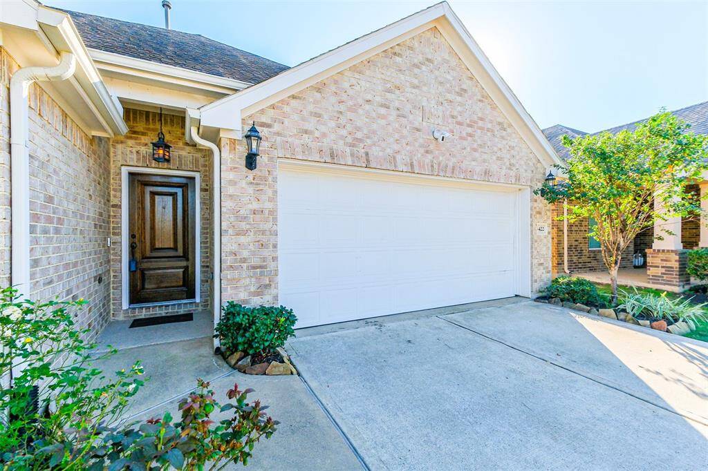 This home features a charming brick exterior with a welcoming front door and a two-car garage. The driveway is spacious, and the entryway is accented by attractive landscaping and outdoor lighting.