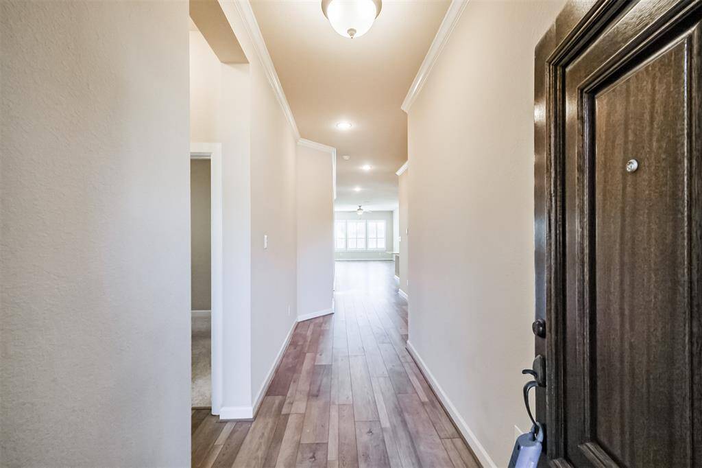 A bright and welcoming entry hallway with wood flooring and neutral walls throughout. This entry leads into an open living area, with a glimpse of a large window framing the outside.