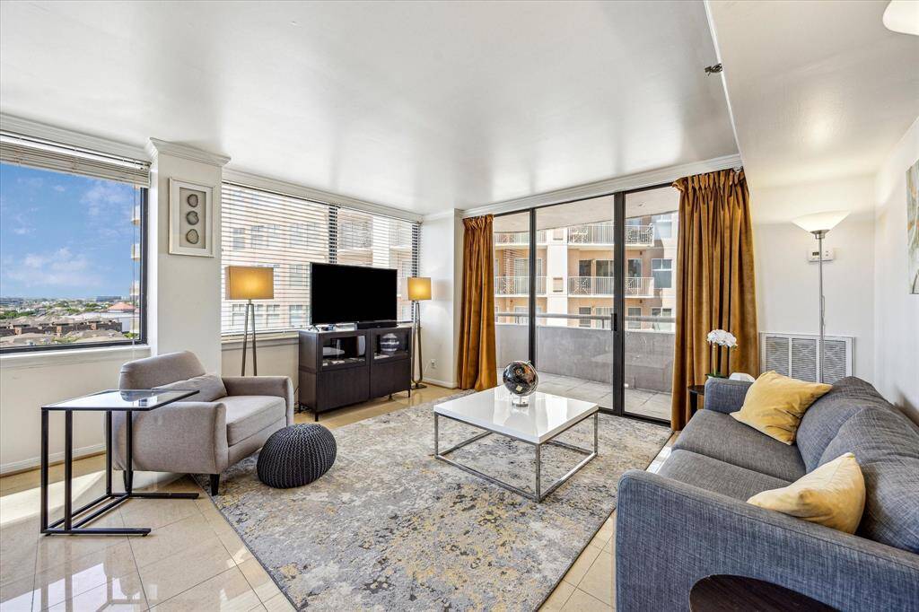 The living room features expansive windows with blinds, sleek tile flooring, and direct access to the balcony.