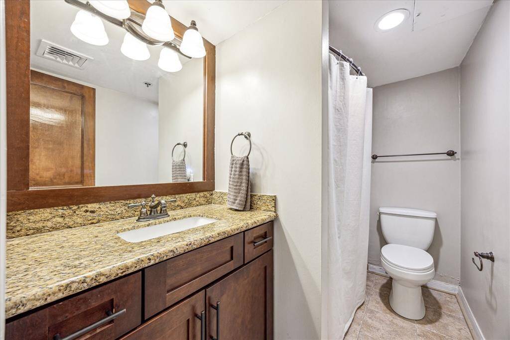 Conveniently located off the foyer is the second full bathroom including granite countertops, a wall mounted mirror with lighting, and a tub in shower.