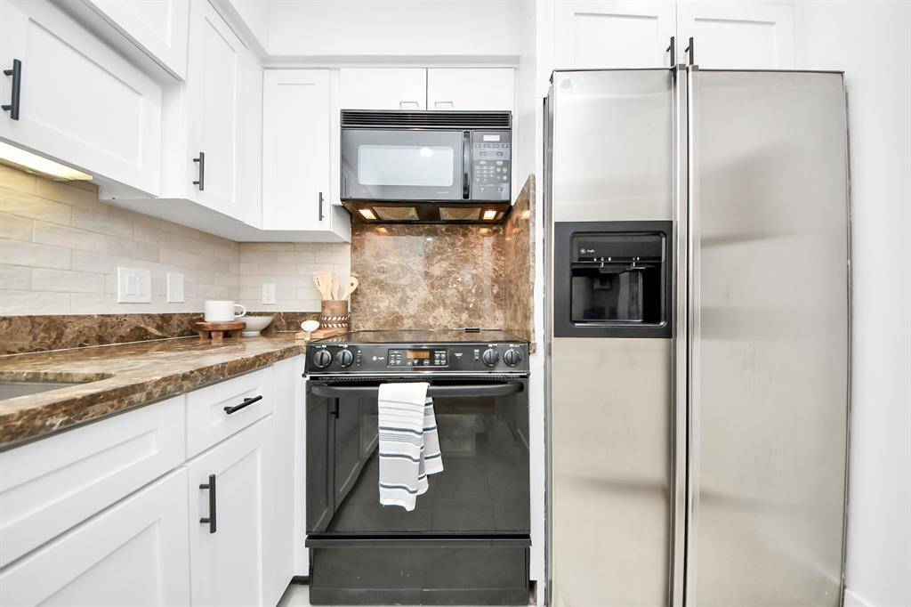 Galley kitchen with white cabinets, marble-style counters and backsplash, and stainless steel appliances including a fridge, range, and microwave.