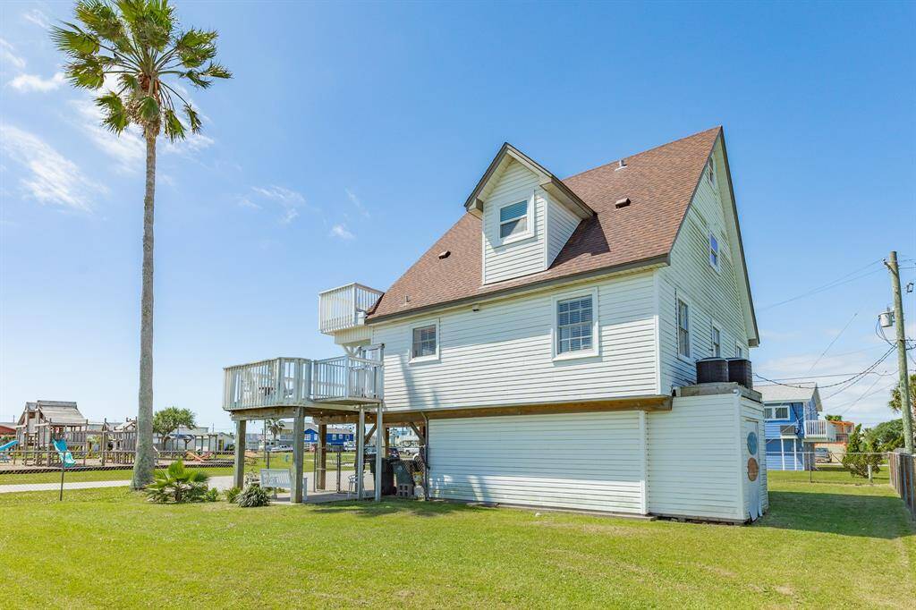 A wide grassy lawn surrounds this raised coastal home with two upper decks and a ground-level patio. Plenty of space to roam, play, or expand outdoor living.